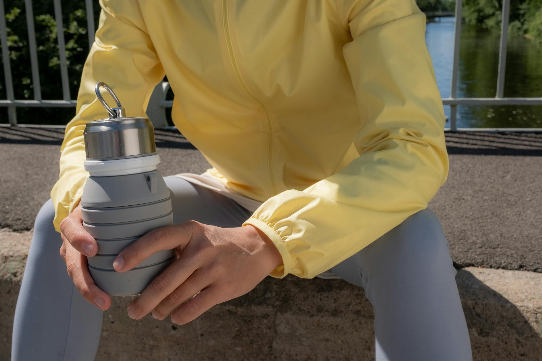 A woman smiling while holding a reusable water bottle outdoors.